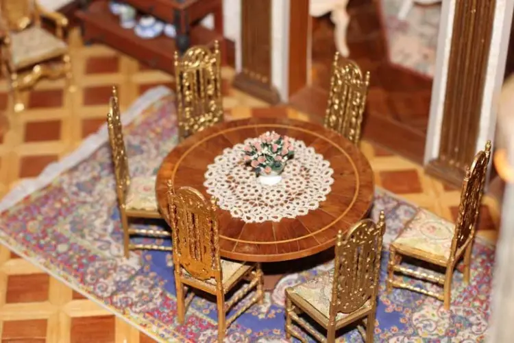 Round dining table with a lace doily and gilded chairs on a patterned rug