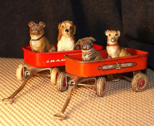Four miniature dogs riding in two red toy wagons