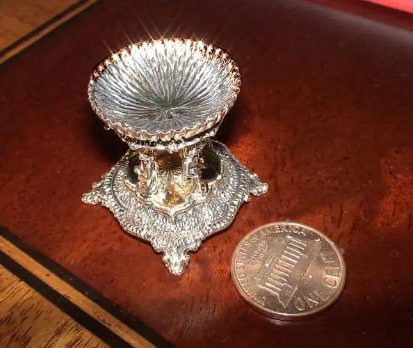 Ornate silver bowl on a stand, next to a penny for scale