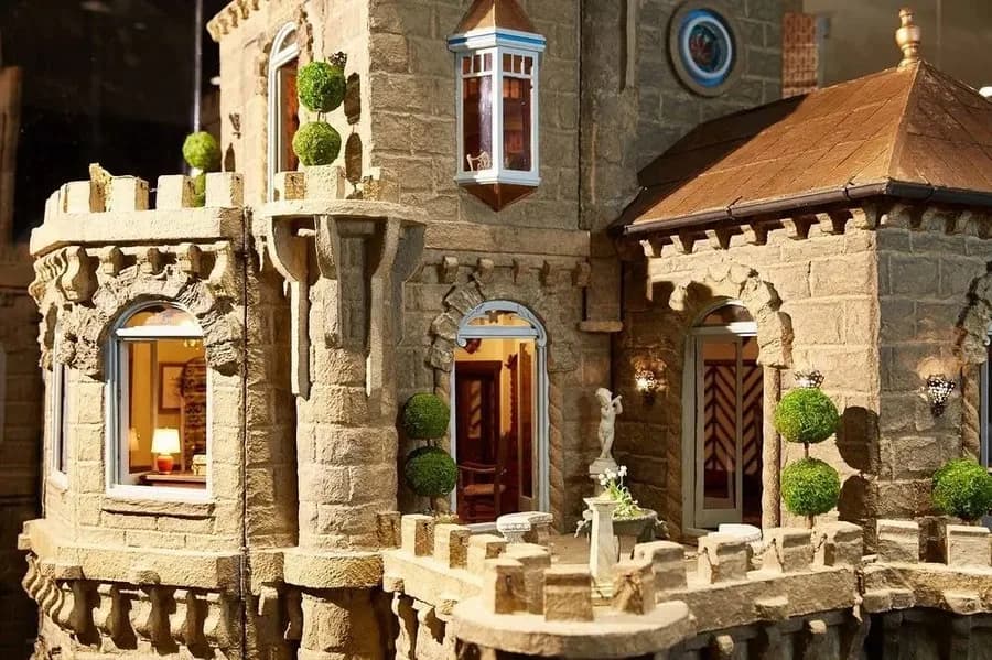 A close-up of the Astolat Dollhouse Castle's stone terrace, topiary, and stained-glass windows